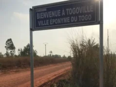 Togoville, l’Incroyable Histoire du Village Qui a Donné Son Nom à Tout Un Pays Une plaque indicatif sur laquelle est écrit : "Bienvenue à Togoville, ville éponyme du Togo". Elle est mise sur une piste en latérite avec la lumière du soleil au-dessus de la plaque. Située à environ 30 km de Lomé, la capitale togolaise, Togoville renferme pourtant des richesses culturelles qui peuvent être mises en valeur pour son développement | Photo: I.K. / BBC