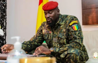 Guinée: Cinq ans de Doumbouya et une « machine répressive affamée » La disparition forcée du magistrat Algassimou Diallo, filmé début septembre dans une prison en Guinée forestière, est un épisode de plus dans la dérive du régime de l’ancien légionnaire français, auteur d’un putsch en 2021. « Algassimou Diallo, détenu à la prison civile de Macenta. » L’homme qui ânonne son nom face caméra, tenue rouge et doigts gigotants, avant de poser droit comme un « I » entre deux lits superposés métalliques, est un magistrat renommé en Guinée. Algassimou Diallo était le procureur du procès du massacre du 28 septembre 2009, très médiatisé. Avant sa déchéance éclair – brutale, serait-on tenté d’écrire –, il avait été affecté à la Cour suprême de Guinée en tant qu’avocat général. Qu’a-t-il fait ? Les accusations portées contre lui, « provocation à la discrimination, à la haine ou à la violence pour discrimination » et « association de malfaiteurs », reposent sur un audio, présenté comme un échange entre le magistrat et l’opposant en exil Cellou Dalein Diallo, prétendument hostile au pouvoir. Malgré les dénégations de ce dernier, qui crie à la fabrication de preuve, Algassimou Diallo a été révoqué illico de ses fonctions par le Conseil supérieur de la magistrature fin août, puis incarcéré à la maison centrale de Coyah, non loin de Conakry. Le 5 septembre, alors que Mamadi Doumbouya se targuait, à l’occasion du 5e anniversaire de son putsch, d’avoir fait du « vivre-ensemble » une « réalité », en référence au recul du « poison » de l’ethnocentrisme, le magistrat était transféré, yeux bandés, dans une prison en Guinée forestière, distante de 700 km. La vidéo du détenu, diffusée au journal de la télévision publique, la RTG, était censée rassurer ses proches, ses collègues et ses avocats, restés sans nouvelles durant plusieurs heures. Plusieurs heures d’inquiétude au cours desquelles ils n’ont pu s’empêcher d’envisager une énième disparition forcée perpétrée par le régime. Des dizaines d’individus en ont été victimes depuis que Mamadi Doumbouya est aux affaires. L’organisation Tournons la page Guinée (TLP-Guinée) a pu documenter trente-cinq cas, et a lancé le 6 août la plateforme memoireguinee.org, en vue de collecter et de vérifier de nouveaux témoignages. La peur du kidnapping par les commandos du pouvoir a été ravivée de façon tragique dans le pays le 24 août. Un charnier contenant six corps, yeux bandés et mains ligotées, a été découvert par des villageois, près de la préfecture de Forecariah. Et à moins de 10 kilomètres d’un camp des forces spéciales, le corps de Mamadi Doumbouya. Kouma Média, composé de journalistes guinéens en exil, avait révélé en mai que le camp abritait un lieu de détention et de torture illégal, réservé aux « enlevés ». Les corps exhumés de ce charnier auraient pu faire l’objet d’« exécutions extrajudiciaires, sommaires ou arbitraires », ont alerté, quant à elles, le 30 août, une vingtaine d’organisations de la société civile africaines. Les autorités ont annoncé une enquête. Mais aucun résultat d’autopsie n’a été rendu public, pas plus que l’identité des individus gisant sous terre. « Qu’il s’agisse de l’incendie du dépôt de carburant de Conakry en décembre 2023, de l’usage excessif de la force dans un stade qui a causé la mort de plus de 140 personnes à N’Zérékoré en décembre 2024, des disparitions forcées, on n’a jamais vu de bilan, de rapport public et encore moins de mesures prises pour que les auteurs répondent de leurs responsabilités », déplore Abdoul Sacko, coordinateur du Forum des forces spéciales de Guinée (FFSG), l’un des très rares « relâchés » après avoir été enlevés puis torturés. Il est actuellement en exil. Ces événements jalonnent le contre-récit des cinq années de pouvoir de Mamadi Doumbouya. Un « mandat » au cours duquel les droits et libertés sont décidément étouffés, méprisés, enterrés, sur fond de musellement de la presse et de dissolution des partis politiques. Concomitamment à l’arrestation d’Algassimou Diallo et à la découverte de cette fosse commune, un autre drame a secoué la Guinée. Dans la nuit du 22 au 23 août, la décharge publique de Dar es-Salam, à deux pas de l’aéroport international de Conakry, s’est effondrée, causant la mort de trente-six personnes. L’événement est survenu le jour de la fermeture programmée du site, dans la cadre d’un projet financé à hauteur de 70 millions d’euros par l’Union européenne et l’Agence française de développement, et prévoyant notamment la construction d’un Centre d’enfouissement moderne, relève le FFSG dans un communiqué. Pourtant, la veille au soir, un bulldozer juché au sommet de la montagne de déchets s’activait encore pour tasser de nouvelles ordures. Ce projet aurait été ralenti et négligé par les autorités, peut-être parce qu’il n’était pas assez rentable à court terme, avance Abdoul Sacko. « Pire, » poursuit-il, le chef de l’État s’est rendu sur les lieux du drame sans aller au chevet des familles de victimes, des blessés, ou des sans-abris. Des opérations de déguerpissement sans processus de relocalisation ont été rapidement conduites dans la foulée. Comme si on ajoutait de la douleur à la douleur, sans tenir compte, à aucun moment, de la vulnérabilité des populations ». Dans son post du 5 septembre sur sa page Facebook, Mamadi Doumbouya n’a rendu hommage qu’aux militaires tombés lors du coup d’État du 5 septembre 2021, en refusant que « la République de Guinée continue de s’abîmer ». Il a par ailleurs, comme à son habitude, évoqué les promesses de Simandou, en référence à l’un des plus grands gisements de fer du monde, dont le minerai est exploité et exporté depuis le mois de janvier. Simandou 2040, censé transformer la richesse minérale en manne pour le développement économique de la Guinée, demeure à ce jour nimbé d’opacité. Aucun programme n’a été publié. La brutalité de la gouvernance de l’ancien légionnaire français, en revanche, est bien concrète. Selon Abdoul Sacko, le cas Algassimou Diallo témoigne d’un énième serrage de vis et envoie le message suivant : « plus personne n’est à l’abri ». « Quand elle aura fini de neutraliser tous les contre-pouvoirs, la machine répressive se tournera vers d’autres acteurs. C’est une machine qui ne peut pas rester sans nourriture, elle est affamée ». TLP-Guinée, de son côté, a dénoncé le 7 septembre dans un communiqué l’irrégularité de la procédure de transfert d’Algassimou Diallo. Et d’alerter : « Tant qu’il n’aura pas été présenté à son juge, à Conakry, en présence de ses avocats et familles, nous considérerons que sa vie est en danger. » A.F. Source: AfriqueXXI.info